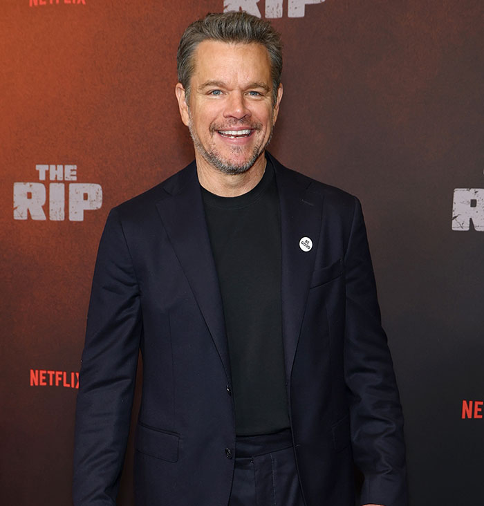 Actor Matt Damon smiling at a Netflix event, wearing a dark suit and black shirt against The Rip backdrop. Actor Matt Damon smiling at a Netflix event, wearing a dark suit and black shirt against The Rip backdrop.
