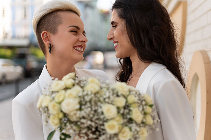 Two brides smiling and holding a bouquet, highlighting estranged relatives demanding access to wedding they were not invited to.
