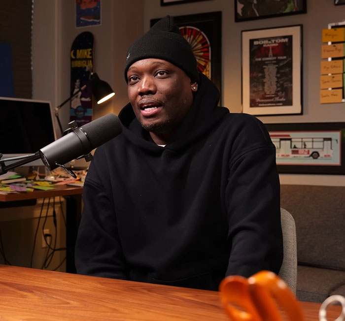 Michael Che wearing black hoodie and beanie speaking into a microphone during a podcast about SNL and ICE debate. Michael Che wearing black hoodie and beanie speaking into a microphone during a podcast about SNL and ICE debate.
