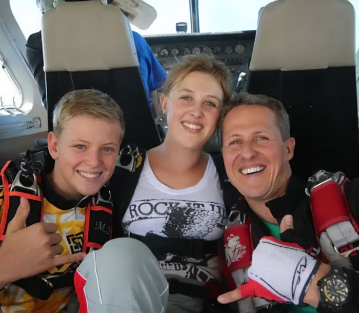 Michael Schumacher giving thumbs up smiling with two young people inside an aircraft before a skydive.