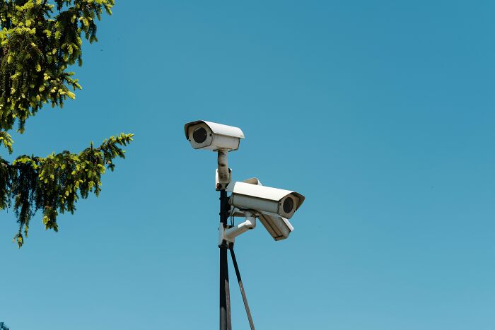 Two security cameras mounted on a pole under a clear sky representing pressing issues in America surveillance.