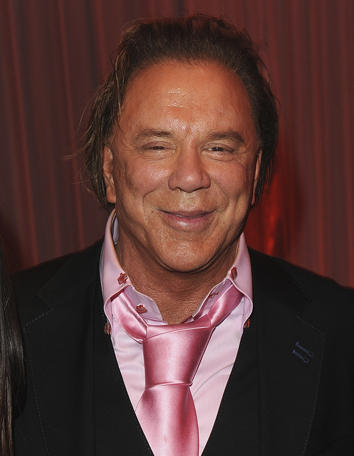 Mickey Rourke attending an event, wearing a pink shirt and tie with a black suit jacket, smiling at the camera.