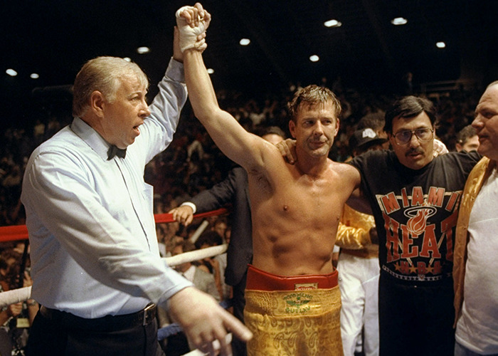 Actor Mickey Rourke with raised arm in boxing ring surrounded by team during post-fight celebration scene.