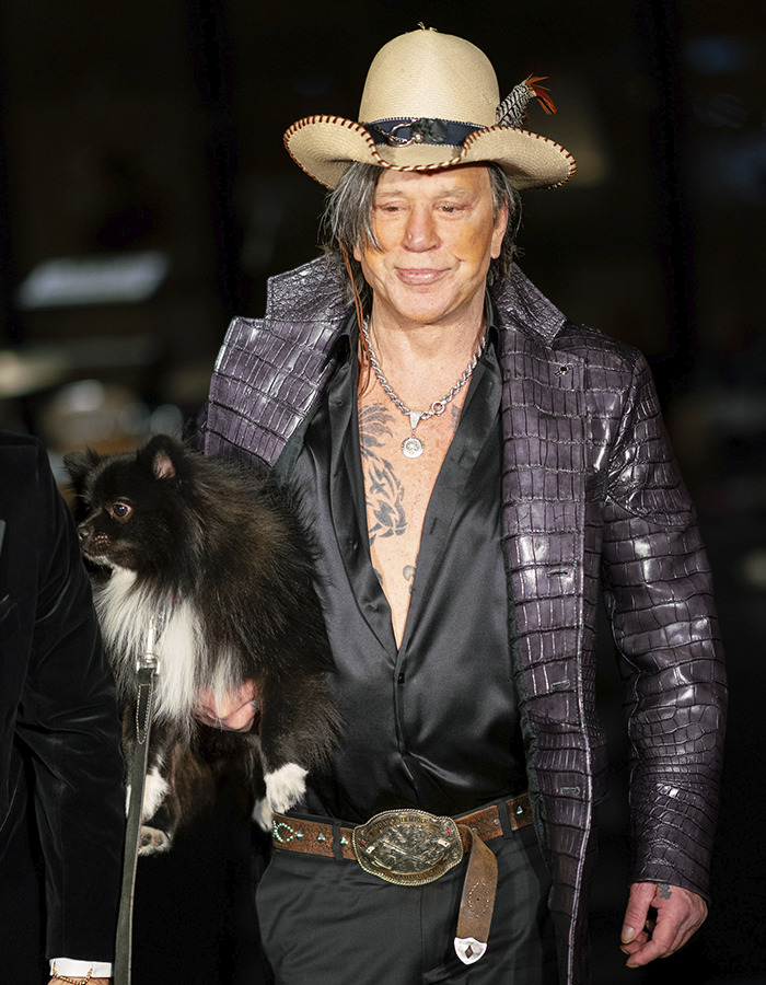 Mickey Rourke wearing a hat and leather jacket holding a small black dog, facing eviction over unpaid rent in LA.