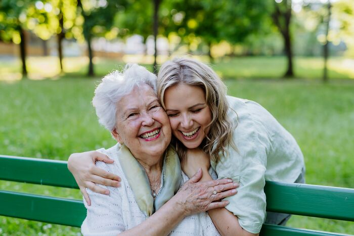 A daughter-in-law and mother-in-law smiling and hugging on a park bench, representing family tensions over racism.