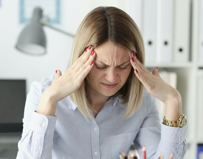 Frustrated woman rubbing temples in an office setting, illustrating tension with racist MIL and upset husband conflict.