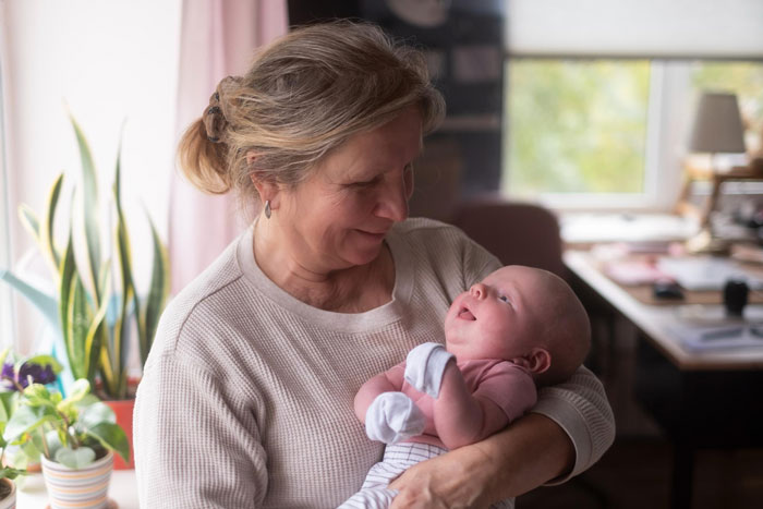 Woman lovingly holding and mil keeps kissing newborn in a cozy, softly lit home environment with plants in background
