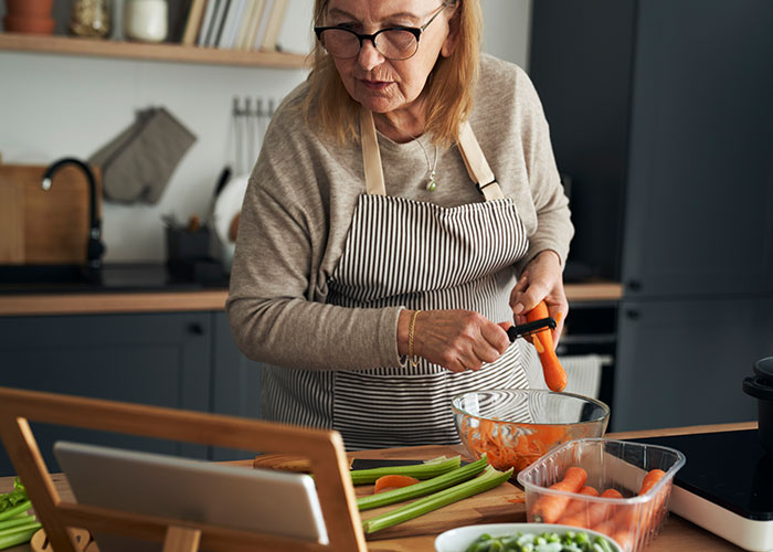 Older woman peeling carrots in a kitchen, illustrating expired food concerns and family meal disagreements.