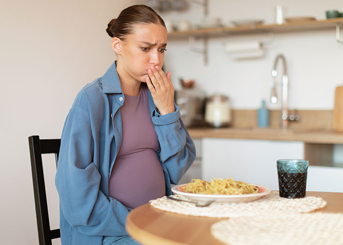 Pregnant woman looking upset at a plate of food in her kitchen, reacting to expired food in her pantry.