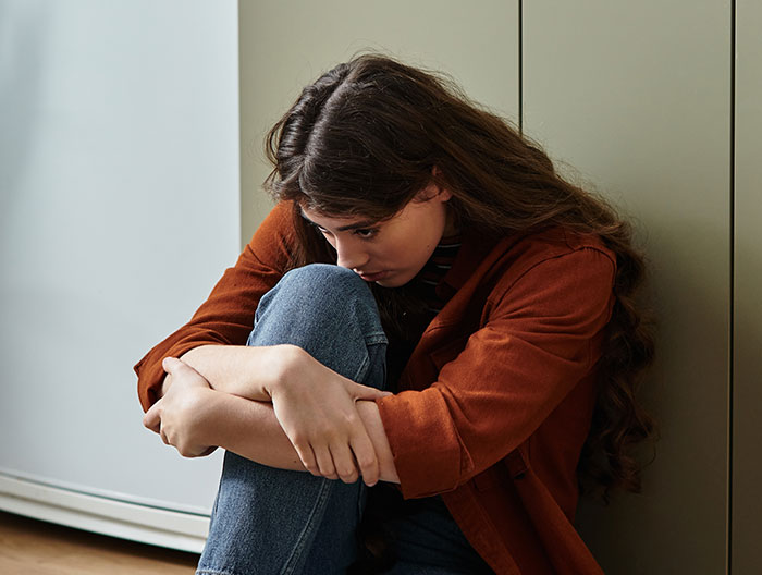 Sad woman hugging knees on floor, representing mom takes her baby and storms off after feeding dispute with MIL