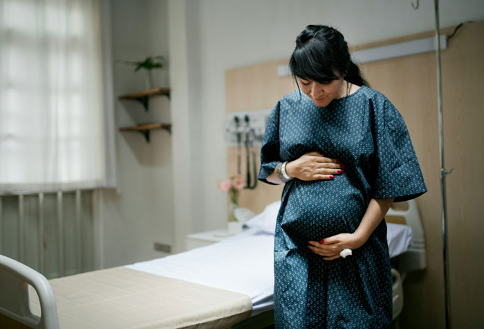 Pregnant woman in hospital gown holding her belly, symbolizing relief and celebration after snapping at controlling vegan friend.