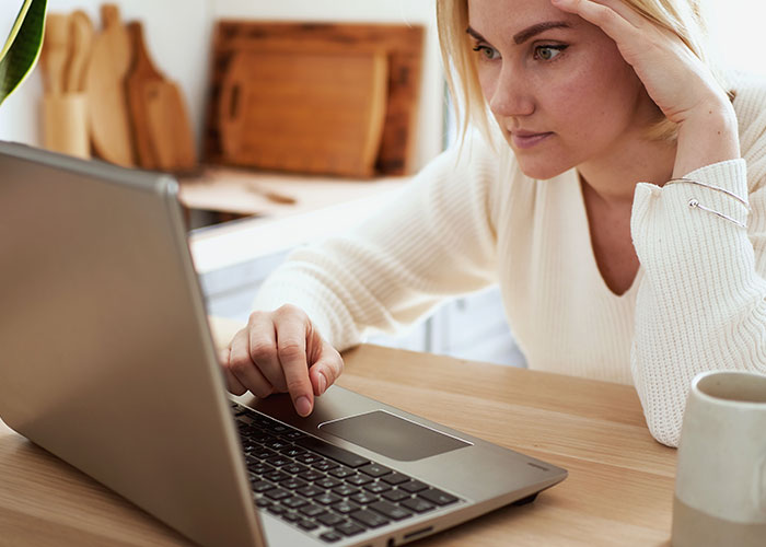 Woman in a white sweater looking concerned while using a laptop, reflecting on mil telling kids parents passed away news.