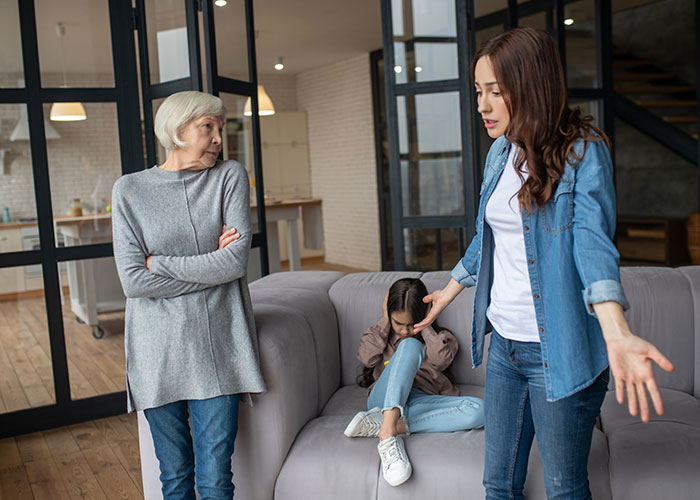 Woman explaining to upset child while elder woman watches, illustrating mil tells kids parents passed away conversation.