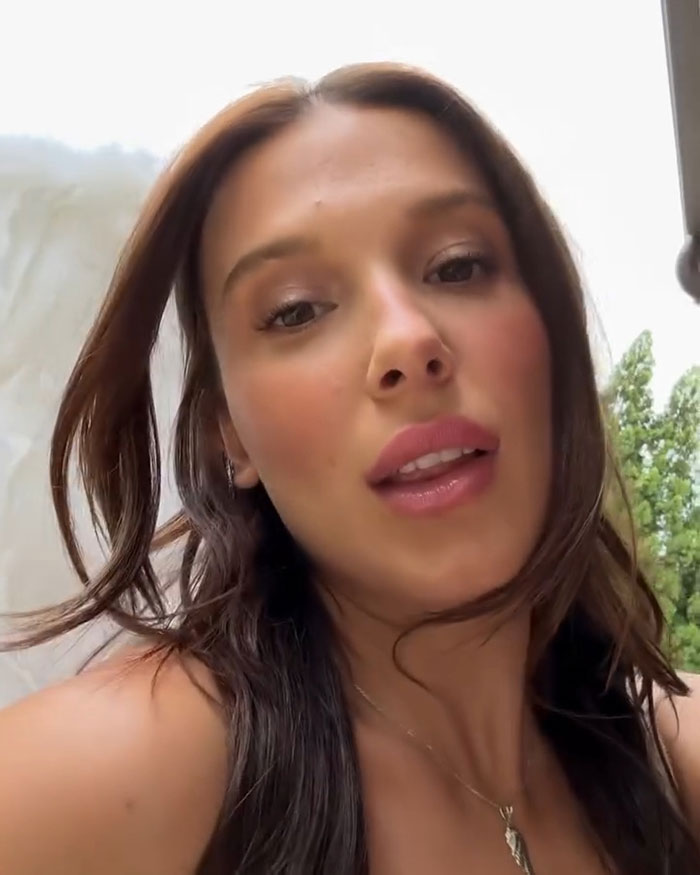 Millie Bobby Brown close-up selfie outdoors with natural makeup and flowing hair, showing her sultry side and grown-up look.