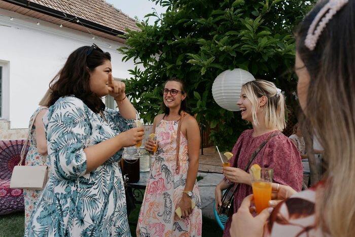 Guests at a b-day party socializing outdoors as a guest mom takes control and rearranges food on the table.