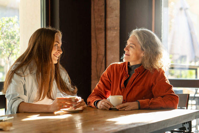 Young woman and her mother having a tense conversation over coffee about managing chores and school burnout.