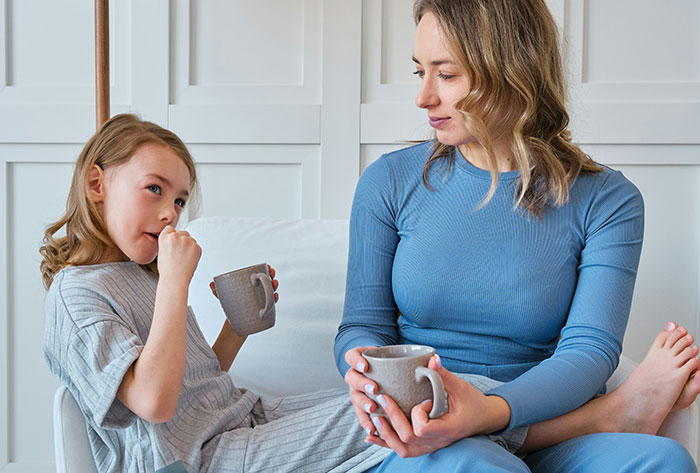 Mother and daughter on couch holding mugs, parent conflicted whether to make daughter attend birthday Mother and daughter on couch holding mugs, parent conflicted whether to make daughter attend birthday