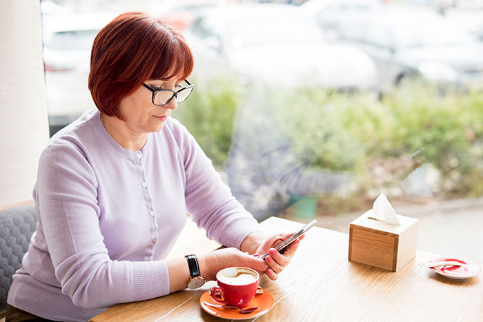 Selfish lady sitting at caf&eacute; table, looking at phone with coffee cup, appearing distant and alone