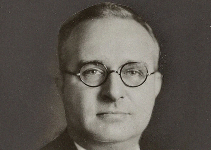 Black and white portrait of a man wearing round glasses, representing people who passed away in ironic ways.