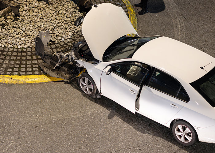 White car crashed into a curb with its hood open, illustrating one of the ironic ways people passed away in accidents.