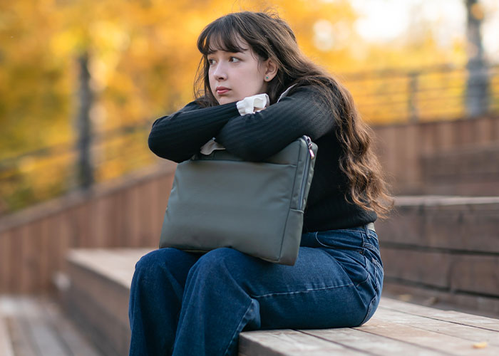 Teenage girl sitting alone on wooden steps in autumn, looking thoughtful and upset amid family divorce conflict.