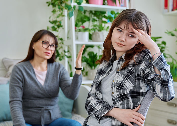 Mother blaming daughter for picking dad in divorce, both sitting indoors with tense expressions during a serious conversation.