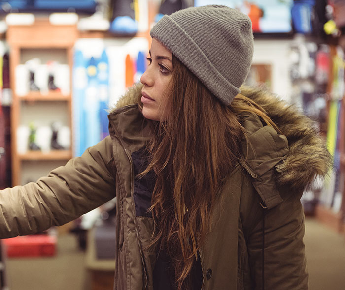 Young woman in a winter jacket and beanie looking concerned with an overwhelming feeling that she needs to leave indoors.