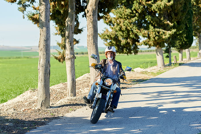 Man wearing helmet riding motorcycle on tree-lined rural road with an overwhelming feeling that he needed to leave