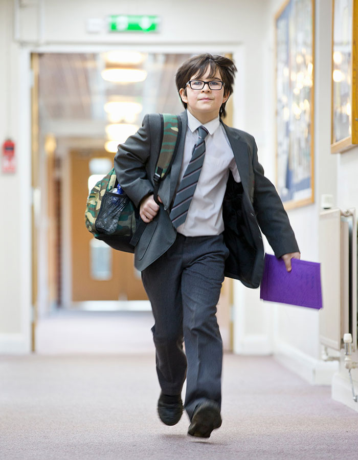 Young boy in school uniform running down hallway with backpack and folder, showing overwhelming feeling that he needed to leave.