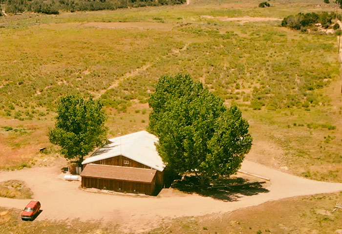 A remote rural house surrounded by trees and open land, evoking a feeling of needing to leave the area.