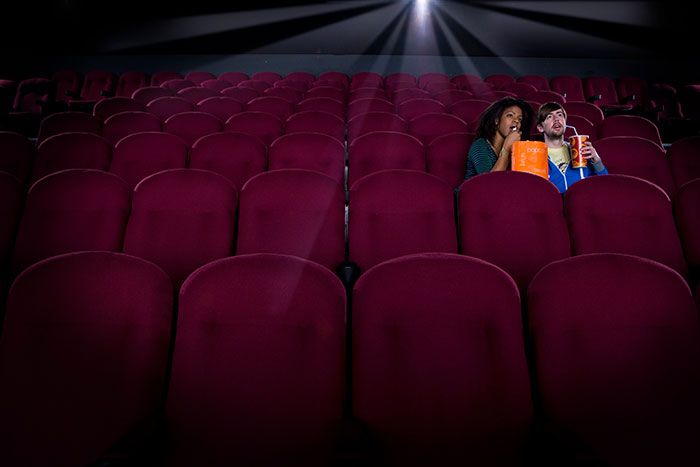 Couple in an empty movie theater looking uneasy, experiencing an overwhelming feeling that they need to leave.