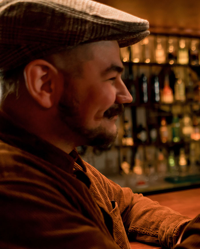 Man wearing a hat sitting at a bar, captured in warm lighting, evoking feelings related to needing to leave situations.