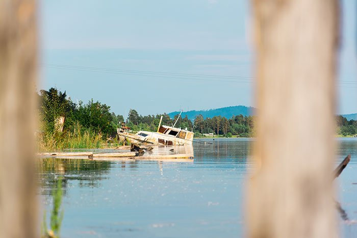 Abandoned boat partially submerged near a calm lake shore, evoking an overwhelming feeling to leave the quiet scene.