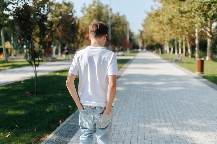 Teen boy walking alone in a park pathway, showing an overwhelming feeling that he needed to leave the scene.