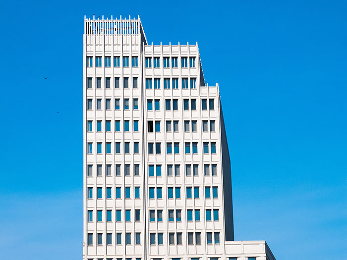 Modern white office building with many windows against a clear blue sky, evoking an overwhelming feeling to leave.
