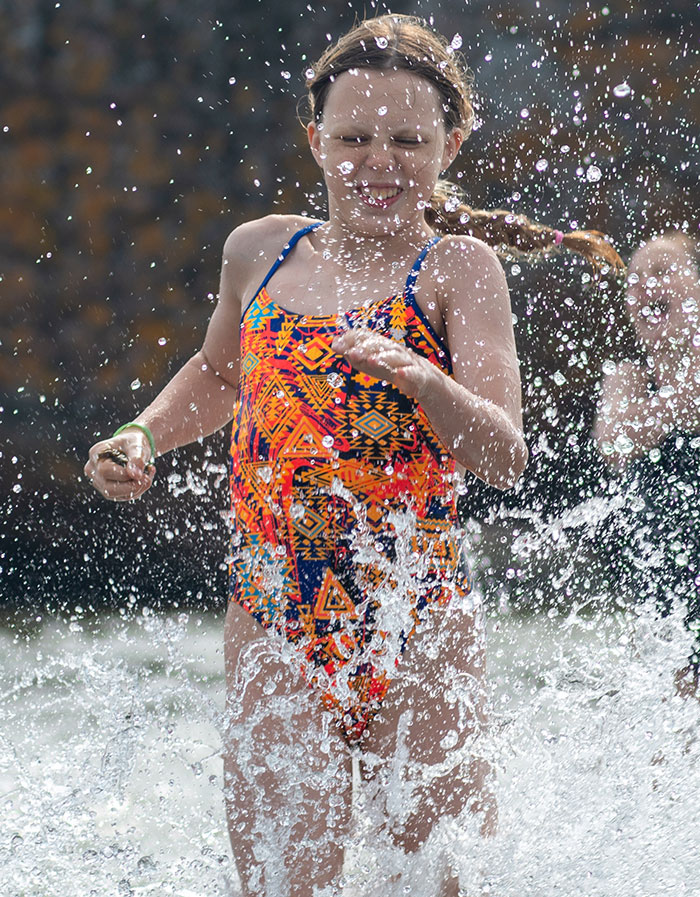 Young girl in colorful swimsuit splashing water, capturing a moment of overwhelming feeling to leave during play.