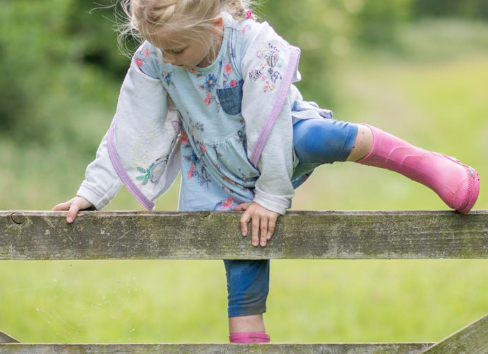 Young girl climbing over a wooden fence in a yard, illustrating neighbor dispute about kids passing through property.