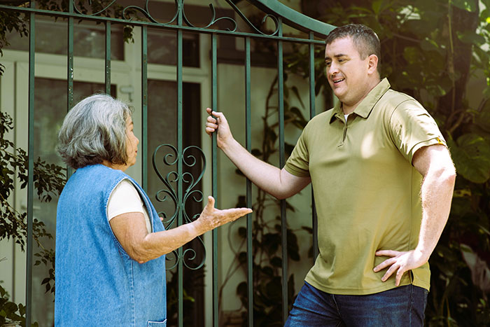 Neighbor and man talking near gate, discussing religious pamphlet with police involvement in a residential outdoor setting