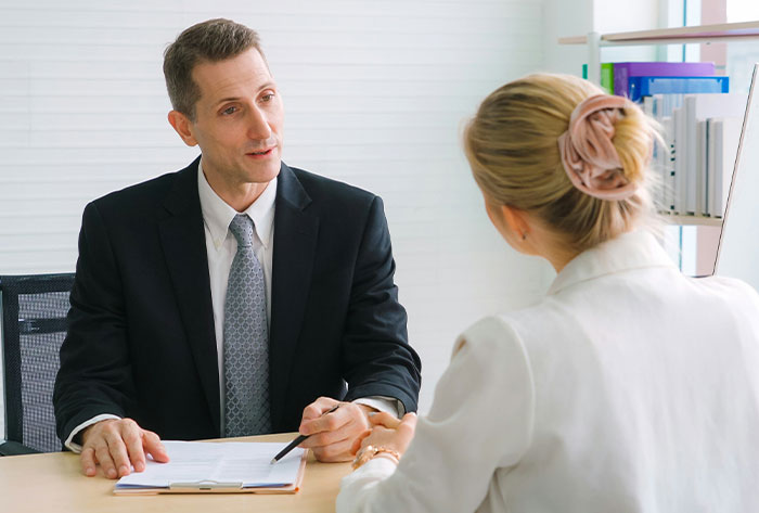 Man in a suit discussing with a woman in a professional office setting about nightmare neighbors and backyard complaints.