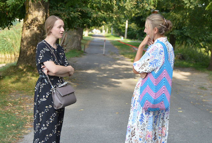 Two women talking on a tree-lined path, illustrating nightmare neighbors complaining about family&rsquo;s backyard use.