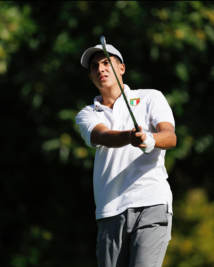 Young golfer in white shirt and cap swinging a club on a sunny day with blurred green trees in the background. Young golfer in white shirt and cap swinging a club on a sunny day with blurred green trees in the background.
