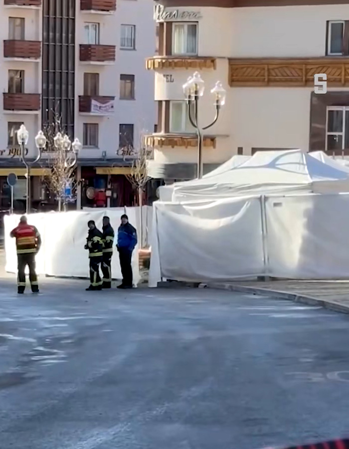 Firefighters and officials near a white tent in a Swiss ski bar area investigating possible cause of lethal fire incident.