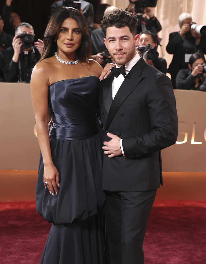 Nick Jonas in a classic black tuxedo walking out of Golden Globes 2026 event with a crowd of photographers in the background.