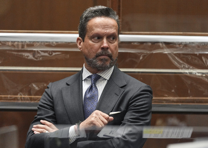 Man in a suit with a patterned tie sitting with arms crossed, reflecting tension after lawyer quits Nick Reiner case.