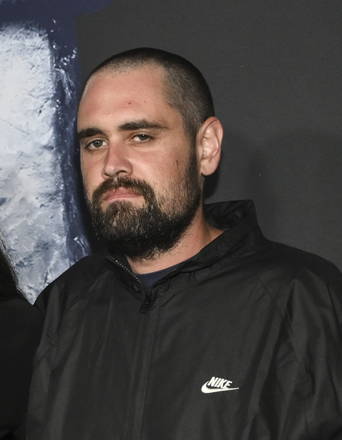 Man with beard wearing a black Nike jacket looking serious in front of a dark background, related to Nick Reiner family update.