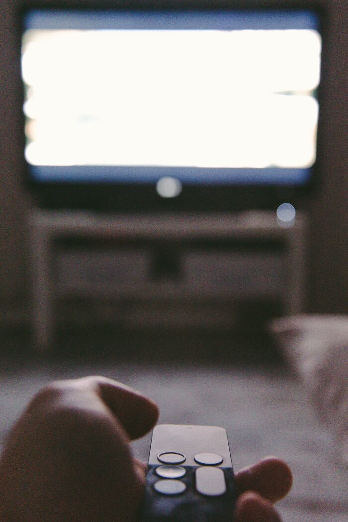 Person holding a remote watching TV indoors, illustrating normal practices in Europe that the US may find weird.