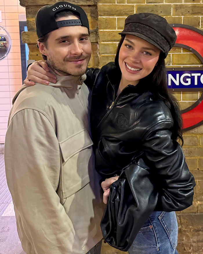 Nicola Peltz smiling in a black leather jacket and hat, showing her tattoo with a pointed message at Beckham family.