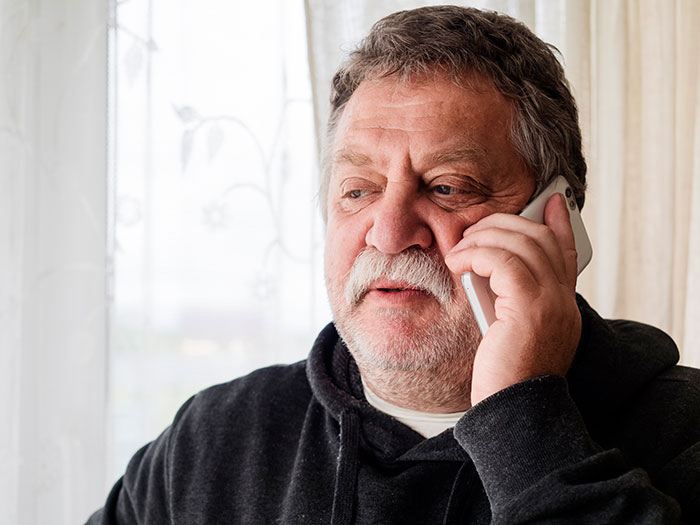 Older man with mustache speaking on phone indoors, illustrating entitled uncle expecting niece to support his retirement plan.