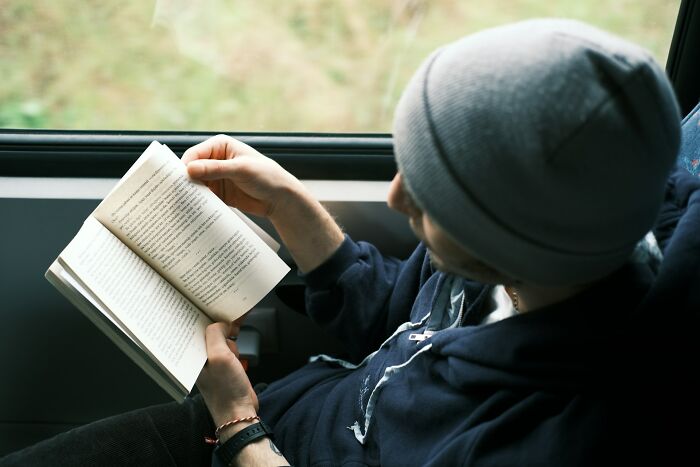 Person wearing a gray beanie reading a book near a window, showcasing moments of surprised intelligence.
