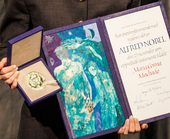 Nobel Peace Prize medal and certificate presented to Maria Corina Machado, highlighted in a close-up photo of hands holding them.